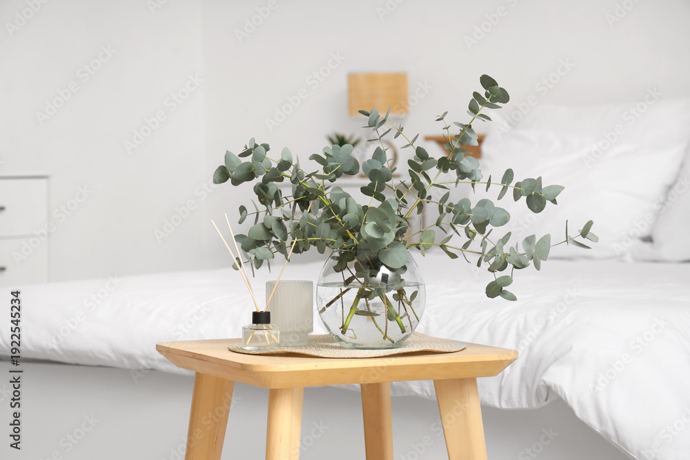 Obraz premium Glass vase with fresh eucalyptus branches on wooden table in bedroom