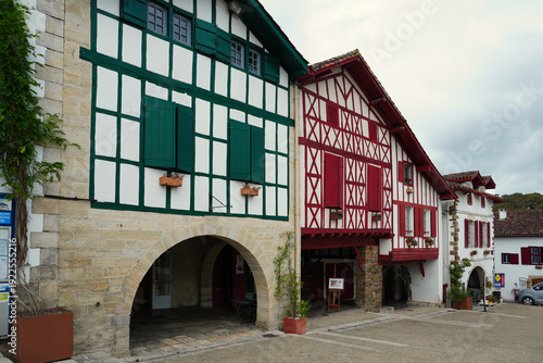 Traditional Basque houses with red timber frames and shutters along a picturesque street in the village of Ainhoa, France. A prime example of Labourd style architecture and cultural heritage