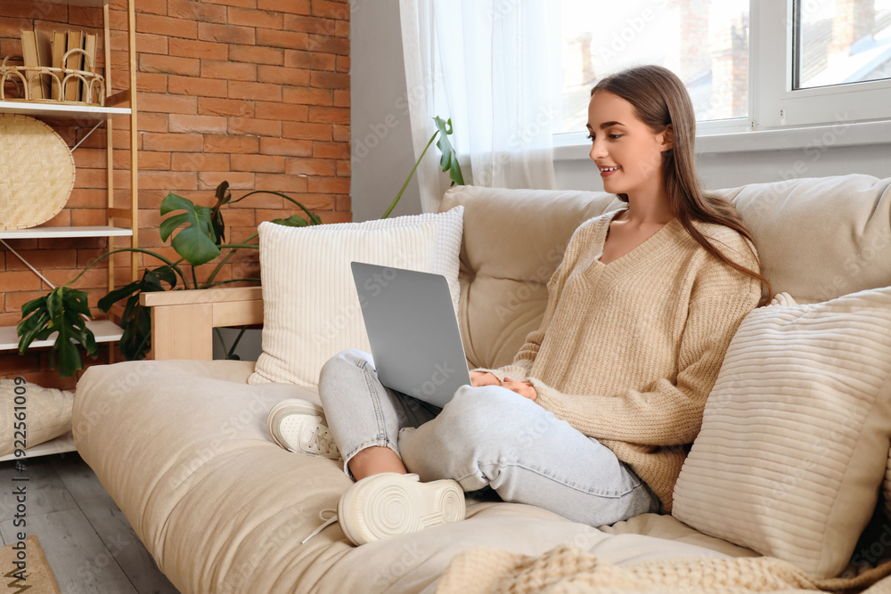 Fototapeta premium Young woman using laptop on beige sofa in living room
