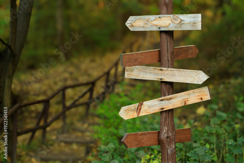 Wooden directional signpost in a forest with multiple weathered planks pointing different ways blurred background of autumn nature