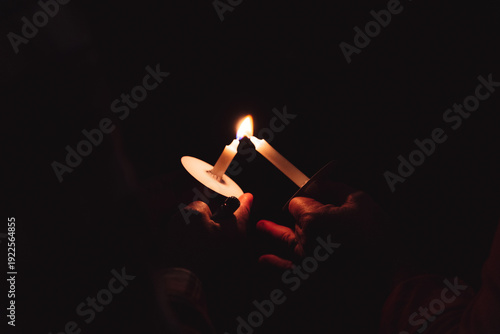Fotografie Hands lighting white candle from another flame in total darkness