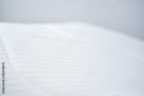 Detailed view of a pristine white quilted mattress protector or topper. The surface shows a subtle pattern of small, raised dots in rows, highlighting its soft texture