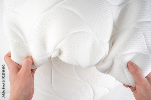 Fotografi Two hands press a white quilted mattress topper, checking its soft elasticity
