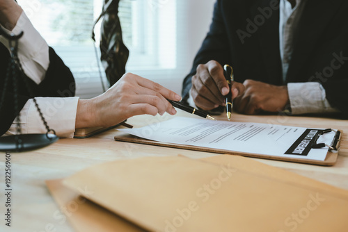 Photos Two lawyers discuss legal documents at a desk, with a scale of justice and gavel symbolizing law, authority, and professional legal consultation in a modern office