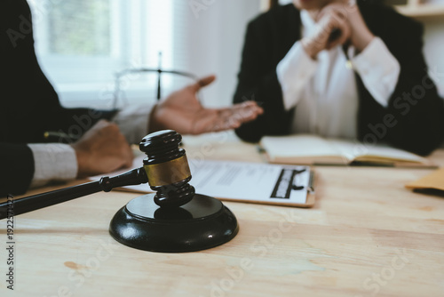 Two lawyers discuss legal documents at a desk, with a scale of justice and gavel symbolizing law, authority, and professional legal consultation in a modern office.