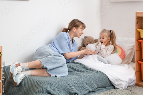 Nanny with little girl and ball lying in bedroom
