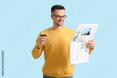 Happy young man with newspaper and cup of coffee on blue background