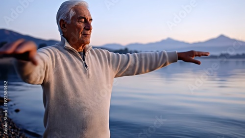 Elderly Caucasian man practicing tai chi by serene lake at dawn, arms extended and hands moving gracefully, mountains and calm water in the background