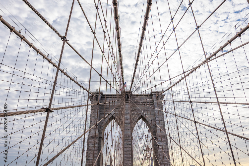 Fototapeta premium Brooklyn Bridge pedestrian walkway perspective with suspension cables and stone towers against cloudy sky in New York City USA