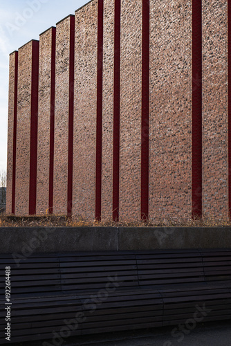 Foto Tall brick facade with red pilasters and wooden bench at plaza