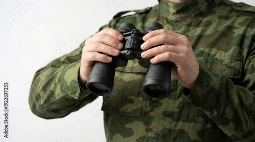 Man torso in green camouflage uniform holding binoculars at eye level on white background with soft studio light and sharp focus on binoculars.
