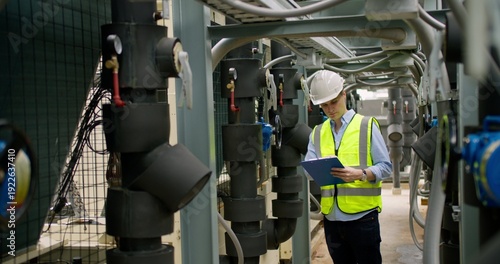 Fotografie Professional industrial engineer is inspecting pipeline machinery in a modern facility, focusing on structural safety, strict quality control and optimizing daily operations