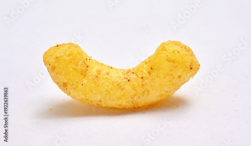 Close-up of a single curved, seasoned yellow corn puff on white background.