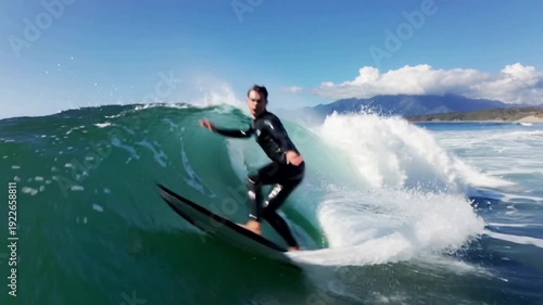 An exciting and dynamic video of a surfer riding powerful ocean waves at the beach. The surfer skillfully balances on the board, gliding smoothly across the sparkling blue water as waves crash and rol