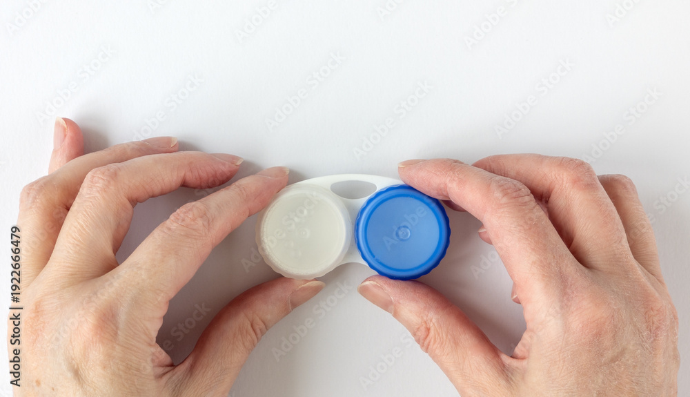 Fototapeta premium Woman's hands holding a contact lens case. Empty white plastic lens case with compartments for storing contact lenses