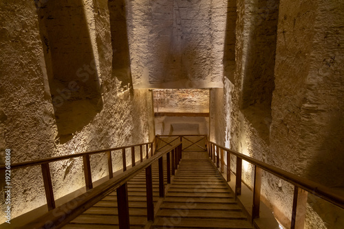 A view down a wooden staircase in an ancient underground structure in the Valley of the Kings with stone walls and subdued lighting.