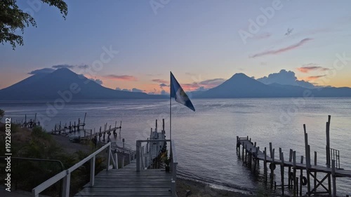 waving Guatemalan flag in front of volcanoes and sunset at Lake Atitlan and boat docks, Panajachel, Guatelmala, Central America