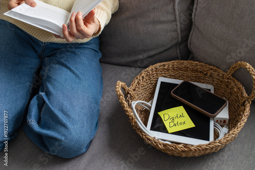 Foto Digital detox concept from woman reading paper book while phone and tablet gadgets lying offline in basket