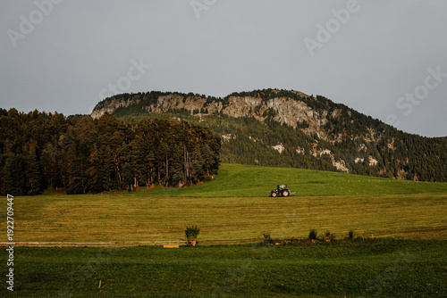Black modern tractor transporting a wrapped silage hay bale on a green mountain meadow in South Tyrol