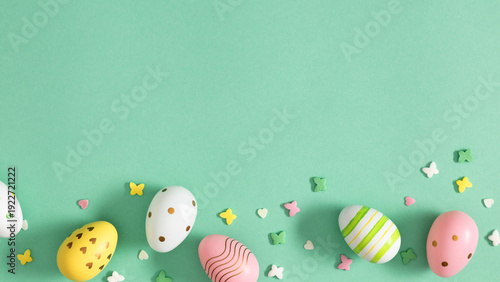 Easter background with colorful pastel eggs and spring decorations on mint green surface, top view flat lay composition with copy space for text, holiday greeting card design concept.