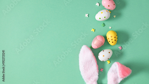 Easter bunny ears with colorful pastel eggs and sprinkles on mint background, flat lay spring holiday celebration composition with copy space for text, top view greeting card design concept.