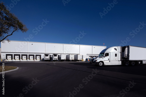 Fotografija storage warehouse with semi-trailers parked at loading docks and a white truck p