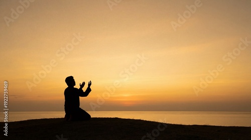 Silhouette of a Muslim man praying on his knees facing the ocean at sunset.