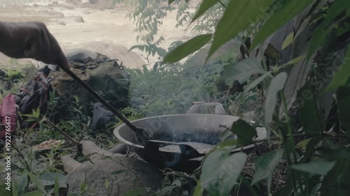 Traditional Fish Frying Over an Open Fire with a Powerful Rushing River Background