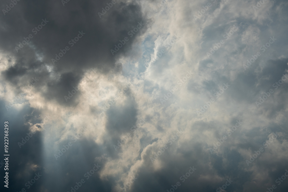 Fototapeta premium Dark gray storm clouds with bright sunbeams breaking through