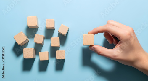 Hand selecting a wooden cube from a group of similar wooden cubes on a blue surface carefully