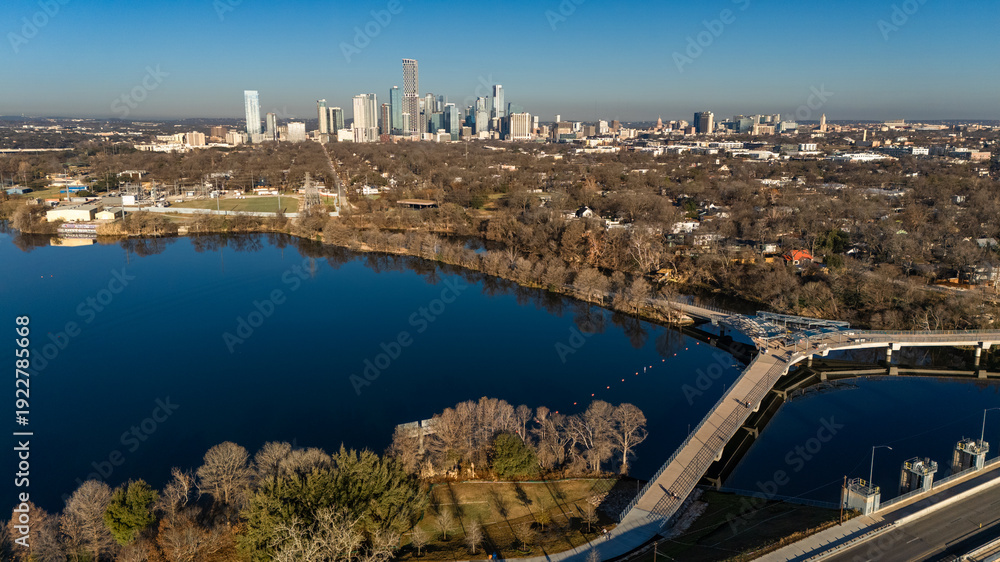 Fototapeta premium Aerial drone photograph showing parkland and shoreline along Lady Bird Lake in East Austin with downtown Austin’s skyline rising beyond. 