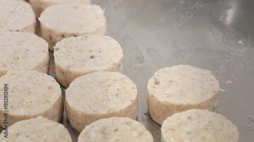 Cook presses minced mixture in firm metal mold producing thick round patty with smooth aromatic texture on tray. Measured compact motion ensures consistent shape for rapid freezing process