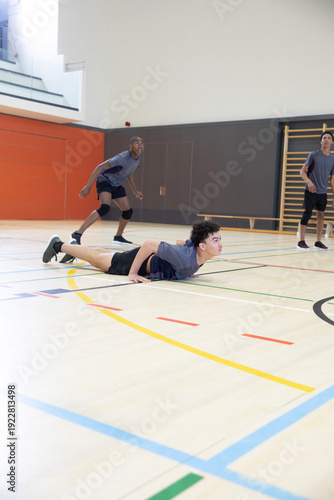 Diverse teenage males practicing on school gym court in gray shirts black shorts knee pads