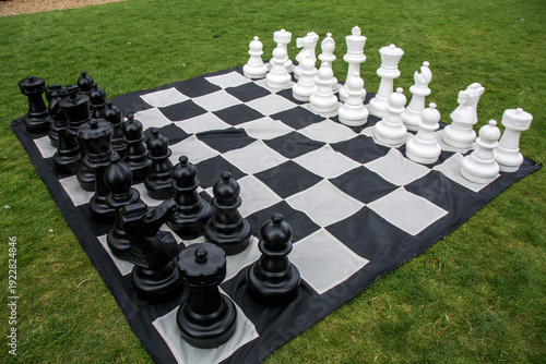 oversized outdoor Chess set arranged on a large black and white checkered mat placed on grass