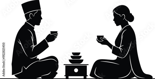 Traditional Muslim couple in silhouette sitting on floor drinking tea wearing songkok and modest dress during Ramadan Iftar or Eid celebration