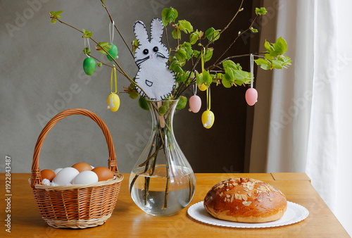 Traditional Czech Easter still life with sweet bread mazanec, wicker basket with eggs and fresh green branches decorated with hanging ornaments on wooden table, festive spring holiday concept