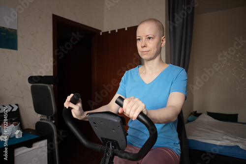 Oncology patient riding exercise bike at home, focused woman rebuilding strength and endurance after chemotherapy, indoor cycling for immunity support, self care and motivation concept