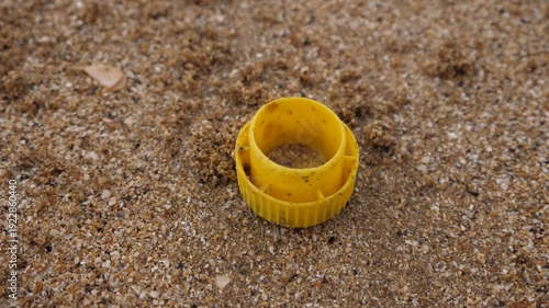 Garbage on the sand of an ocean beach in France, a yellow bottle cap