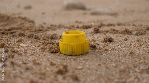Garbage on the sand of an ocean beach in France, a yellow bottle cap