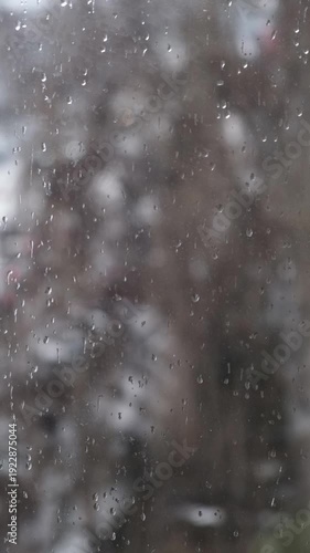 A cinematic 4K vertical (9:16) rainy scene through a window, with sharp raindrops in focus and a softly blurred background.