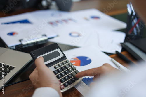 Businessman, accountant, financier using calculator to work through financial documents, report, charts and data on desk