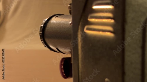 A vintage film projector whirs as it feeds a celluloid strip through its lens. The soft, warm glow from the machine creates a nostalgic and peaceful atmosphere in the dim room.
