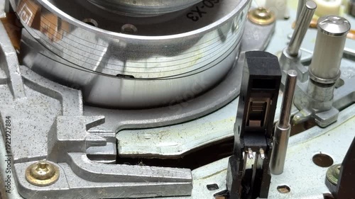 The polished metal VCR head drum rotates at high speed against magnetic tape. This motion creates a consistent, mechanical whirring sound and a subtle high-pitched metallic hum.