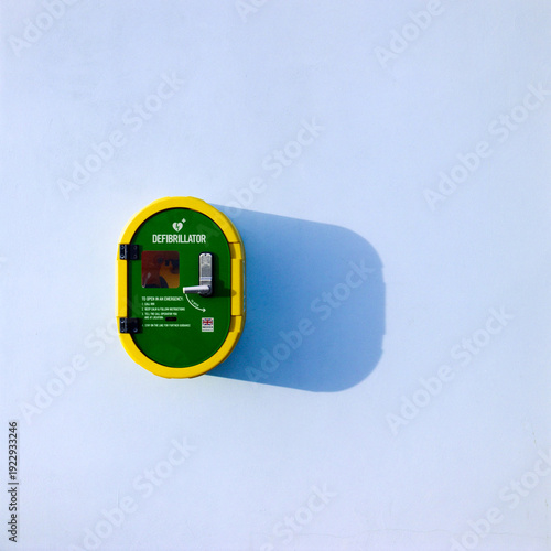 Defibrillator safe, defib safe, on a plain blue wall outdoors with a shadow, life saving equipment, public access defibrillator