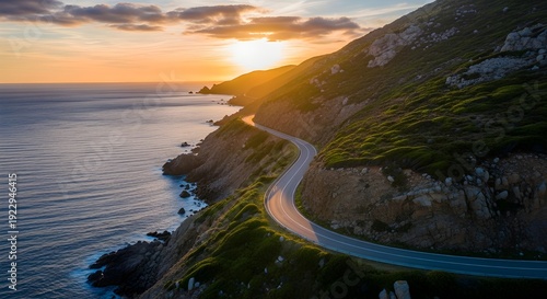 Breathtaking Aerial View of a Winding Coastal Highway Hugging Steep Cliffs Beside the Blue Ocean During a Radiant Golden Hour Sunset with Lens Flare.