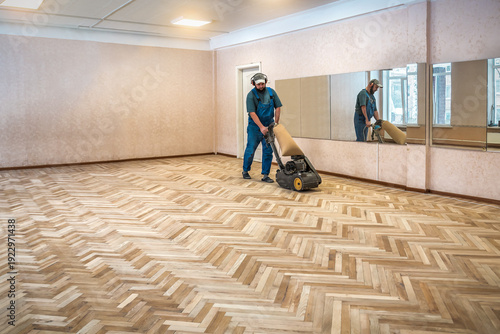 Фотография Carpenter worker is sanding polishing wooden parquet floor during renovation