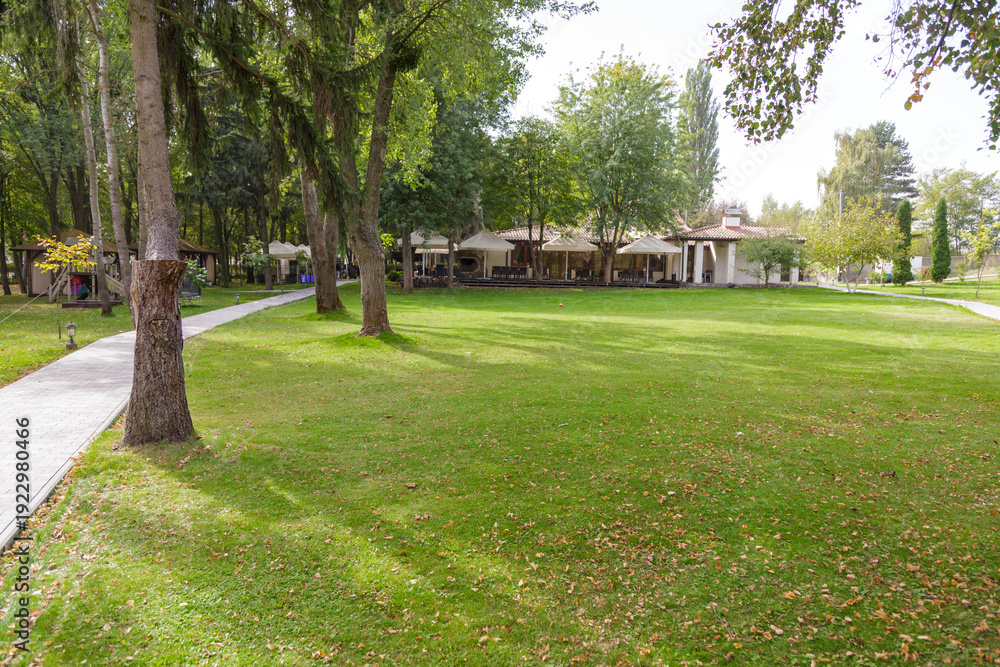 Obraz premium Spacious green lawn near calm lake with trees and pathway, peaceful outdoor recreation and corporate retreat location.