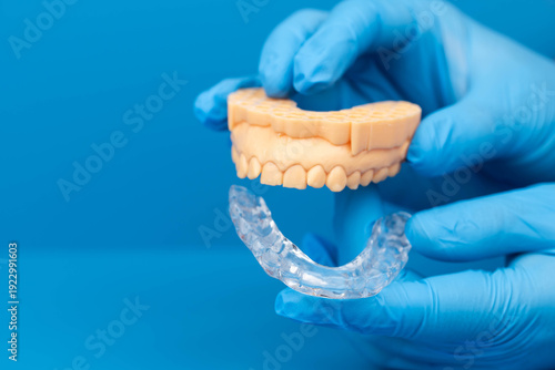 Custom transparent dental night mouth guard for night sleep, bruxism and teeth grinding prevention, orthodontic protection device fitted  on teeth model, orthodontic device. Blue background