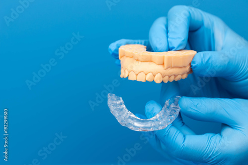 Custom transparent dental night mouth guard for night sleep, bruxism and teeth grinding prevention, orthodontic protection device fitted  on teeth model, orthodontic device. Blue background