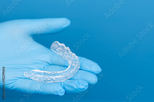 Dentist hands in gloves holding transparent dental mouth guard for night sleep, bruxism and teeth grinding prevention, orthodontic protection device on blue background, medical care and hygiene